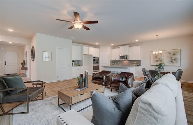 living room with baseboards, ceiling fan with notable chandelier, and light wood-type flooring