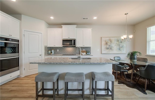 kitchen featuring a kitchen bar, appliances with stainless steel finishes, tasteful backsplash, a sink, and a chandelier