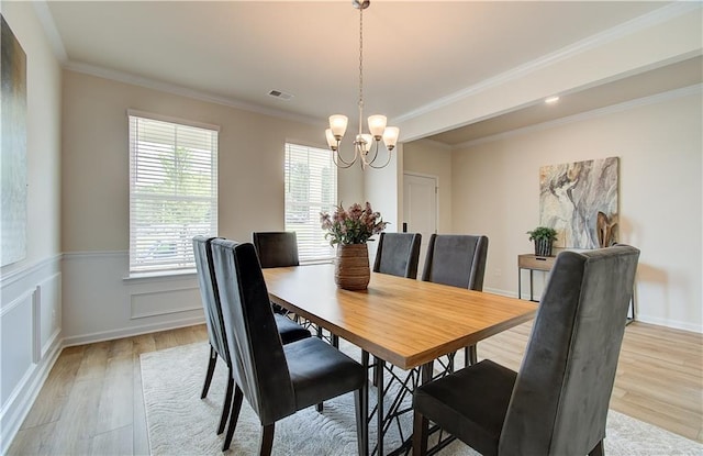 dining space featuring visible vents, ornamental molding, a wainscoted wall, light wood finished floors, and a notable chandelier