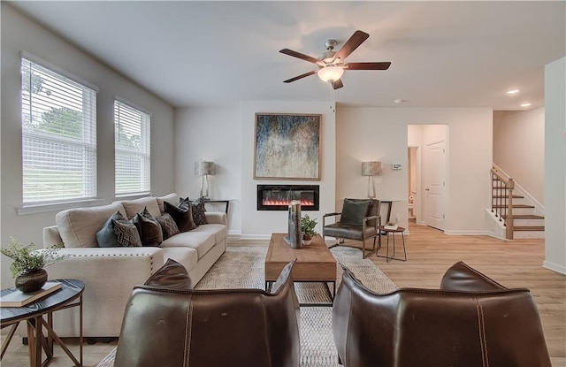living area with a glass covered fireplace, baseboards, recessed lighting, a ceiling fan, and light wood-style flooring