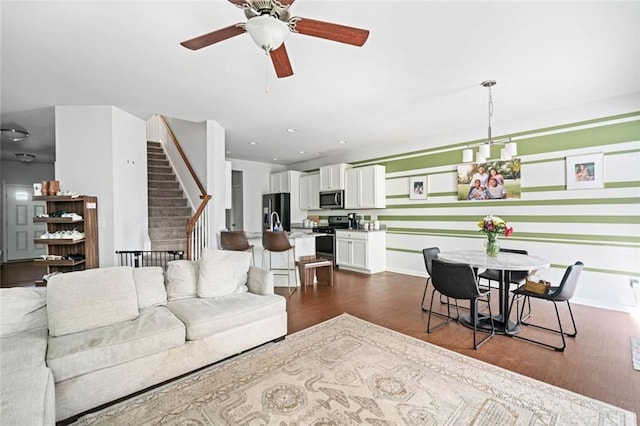 living room featuring baseboards, a ceiling fan, stairs, and dark wood-style floors