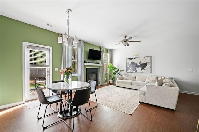 living area featuring a glass covered fireplace, ceiling fan, wood finished floors, and visible vents