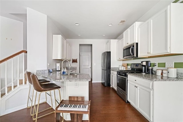 kitchen with a peninsula, white cabinetry, a sink, dark wood finished floors, and stainless steel appliances