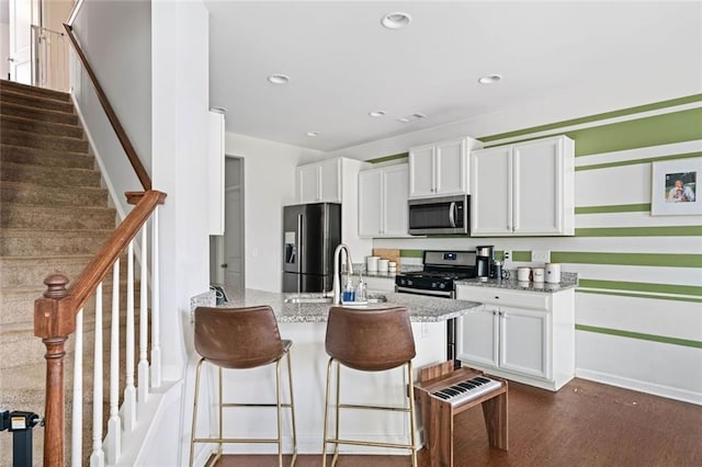 kitchen featuring a peninsula, a breakfast bar area, white cabinetry, light stone counters, and stainless steel appliances