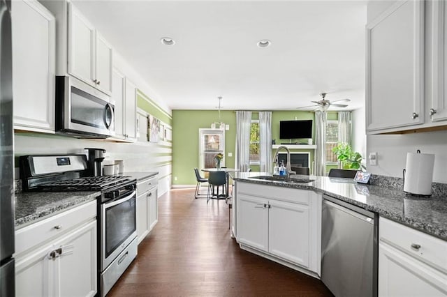 kitchen featuring ceiling fan, appliances with stainless steel finishes, a sink, a fireplace, and a peninsula