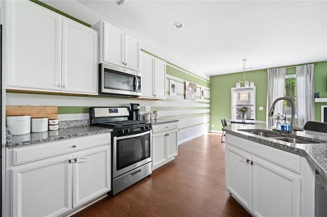 kitchen with appliances with stainless steel finishes, a sink, stone countertops, white cabinetry, and dark wood-style floors
