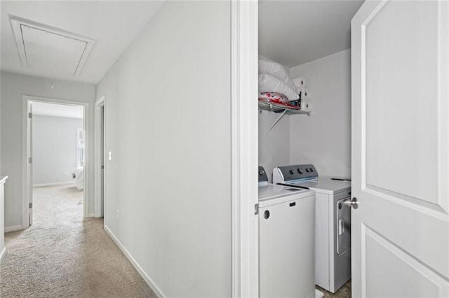 clothes washing area featuring laundry area, light carpet, baseboards, attic access, and washing machine and clothes dryer