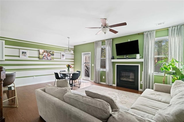 living area featuring visible vents, a glass covered fireplace, wood finished floors, baseboards, and a ceiling fan