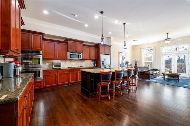 kitchen with a breakfast bar area, stainless steel appliances, open floor plan, a center island with sink, and pendant lighting