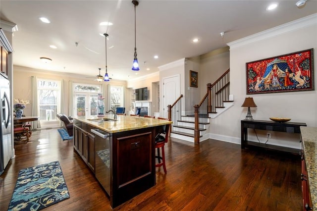 kitchen with an island with sink, light stone counters, hanging light fixtures, a fireplace, and a sink