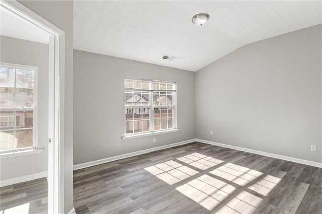 empty room featuring a textured ceiling, a wealth of natural light, dark hardwood / wood-style floors, and vaulted ceiling