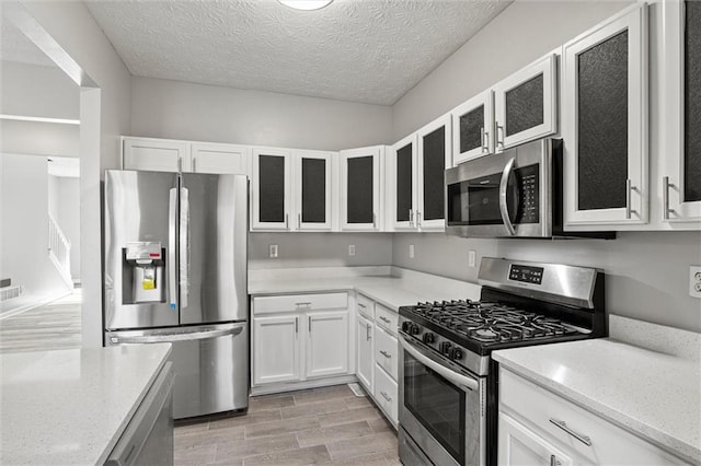 kitchen with appliances with stainless steel finishes, a textured ceiling, light hardwood / wood-style flooring, and white cabinetry