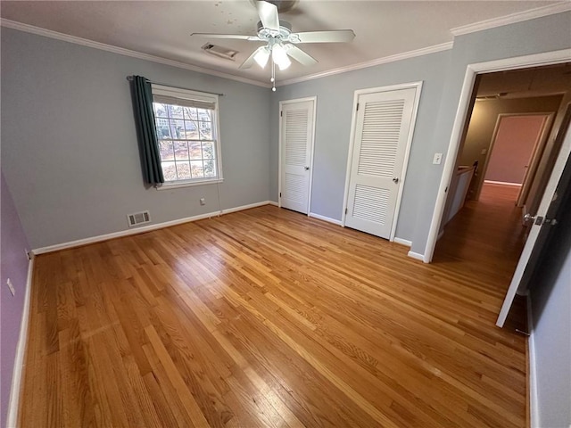 unfurnished bedroom featuring visible vents, light wood-style flooring, multiple closets, and crown molding