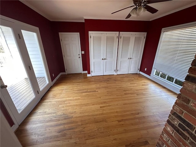 unfurnished bedroom featuring baseboards, ornamental molding, two closets, and light wood-style flooring