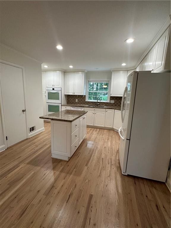 6542 Cherry Tree Ln, Atlanta, GA 30328 - kitchen with freestanding refrigerator, multiple ovens, white cabinets, light wood-style flooring, and tasteful backsplash