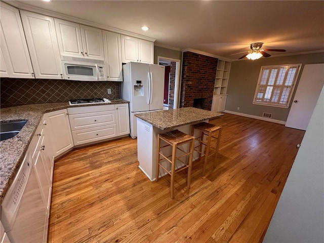 kitchen with a breakfast bar, white appliances, light wood-style flooring, a ceiling fan, and ornamental molding