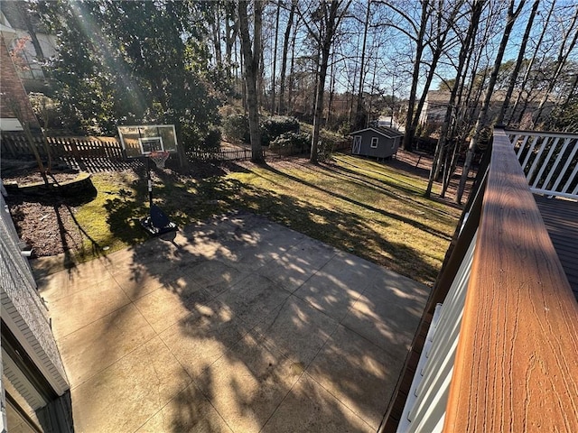 wooden terrace featuring a lawn, an outdoor structure, a fenced backyard, and a patio area
