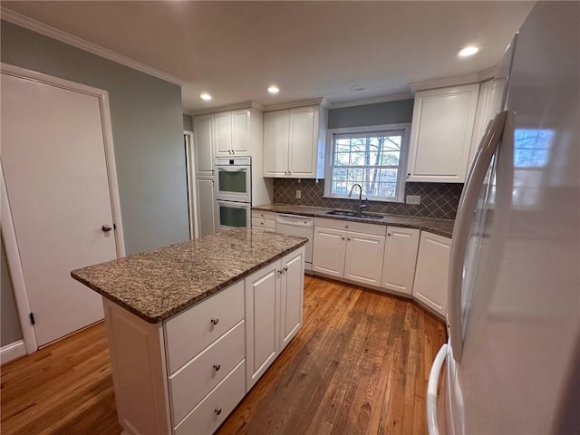 kitchen featuring a sink, ornamental molding, white appliances, and wood finished floors