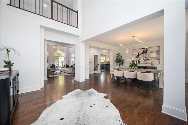 foyer featuring a towering ceiling, dark hardwood / wood-style floors, a chandelier, and ornate columns