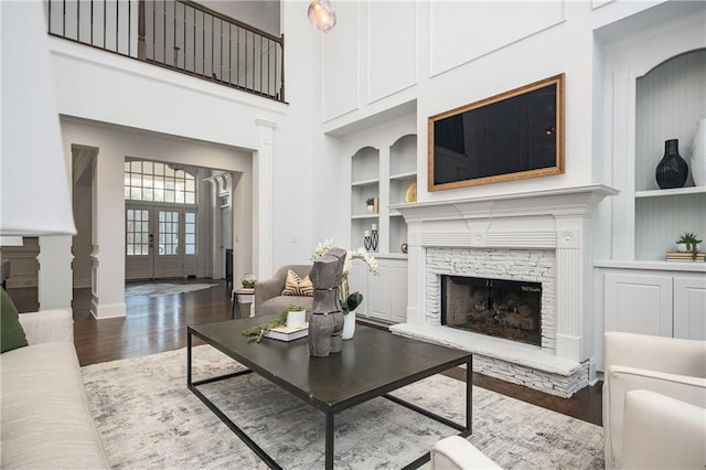 living room with built in shelves, dark wood-type flooring, french doors, a stone fireplace, and a high ceiling