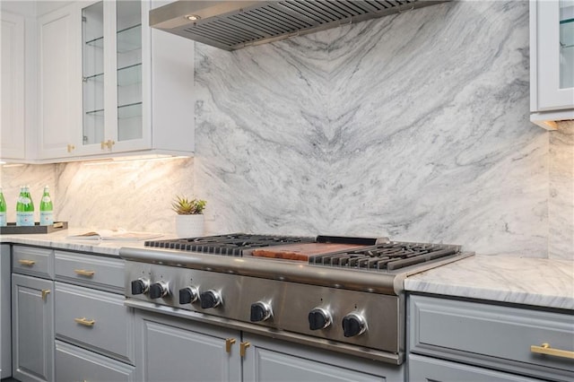 kitchen with custom exhaust hood, tasteful backsplash, light stone counters, gray cabinets, and stainless steel gas stovetop