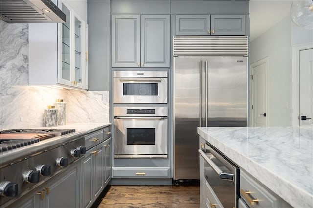 kitchen featuring gray cabinets, light stone countertops, appliances with stainless steel finishes, and custom range hood