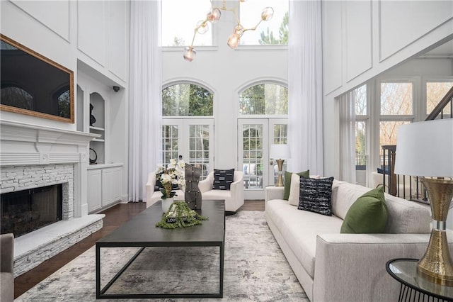 living room featuring a towering ceiling, built in features, a fireplace, dark hardwood / wood-style flooring, and french doors