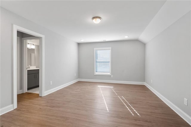 unfurnished bedroom featuring connected bathroom, vaulted ceiling, and hardwood / wood-style flooring