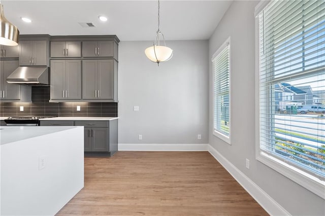 kitchen featuring exhaust hood, gray cabinets, backsplash, pendant lighting, and light hardwood / wood-style floors