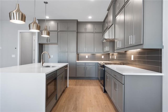 kitchen featuring stainless steel stove, light wood-type flooring, pendant lighting, gray cabinets, and sink