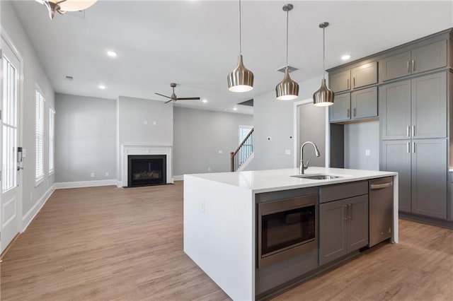 kitchen with a center island with sink, sink, built in microwave, pendant lighting, and light wood-type flooring