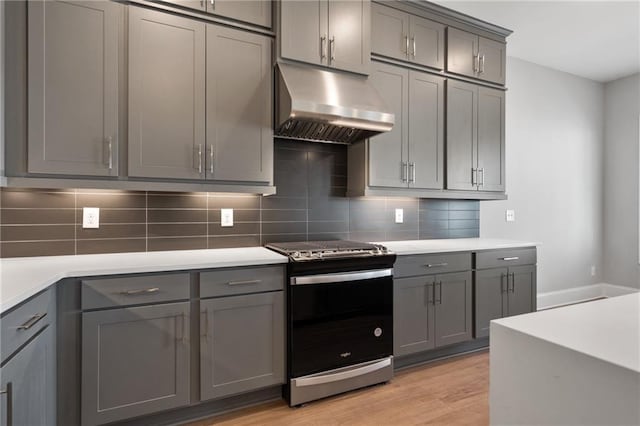 kitchen with gray cabinets, decorative backsplash, light hardwood / wood-style flooring, and stainless steel stove