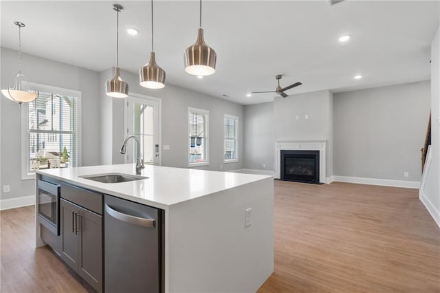 kitchen featuring appliances with stainless steel finishes, sink, light hardwood / wood-style floors, pendant lighting, and a center island with sink