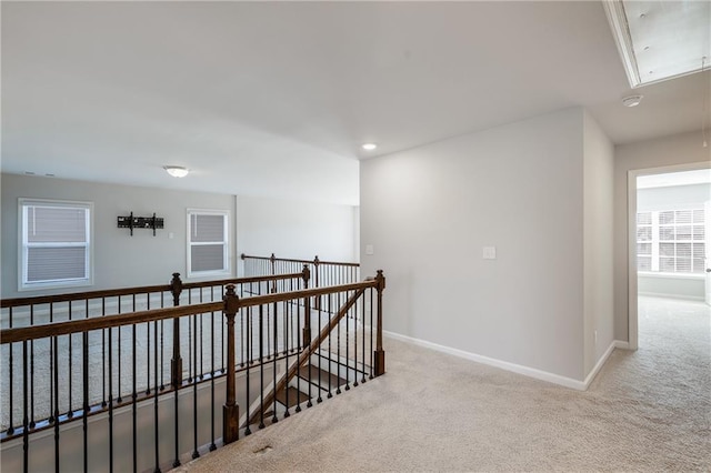 hallway featuring carpet floors, an upstairs landing, attic access, and baseboards