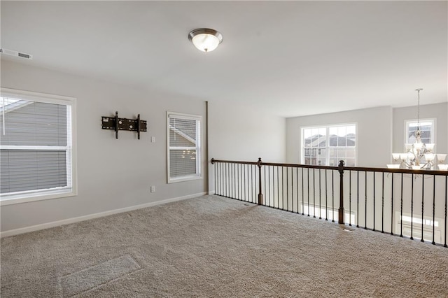 unfurnished room with carpet floors, visible vents, a chandelier, and baseboards