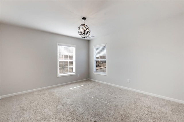 carpeted spare room featuring baseboards and a notable chandelier