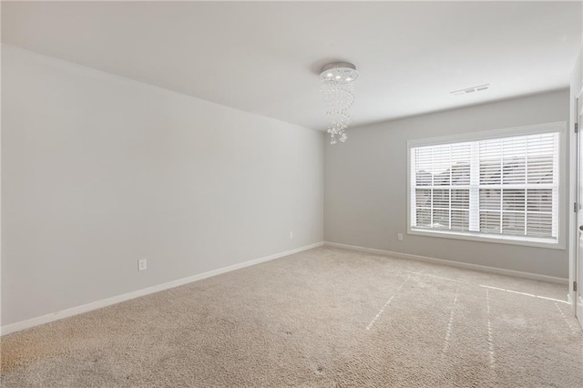 empty room with baseboards, an inviting chandelier, visible vents, and light colored carpet