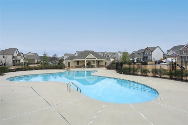 community pool with a patio, fence, and a residential view