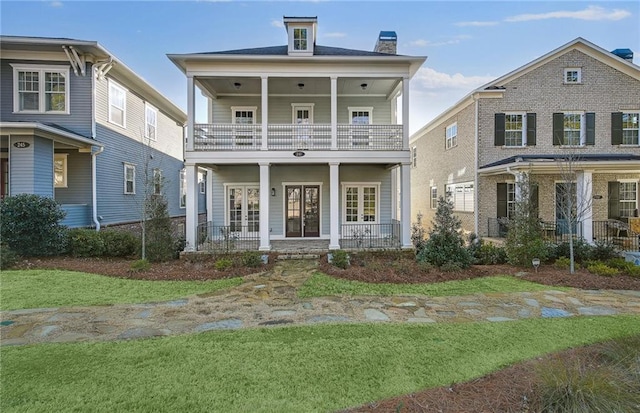 view of front facade with a balcony, french doors, a porch, and a front lawn