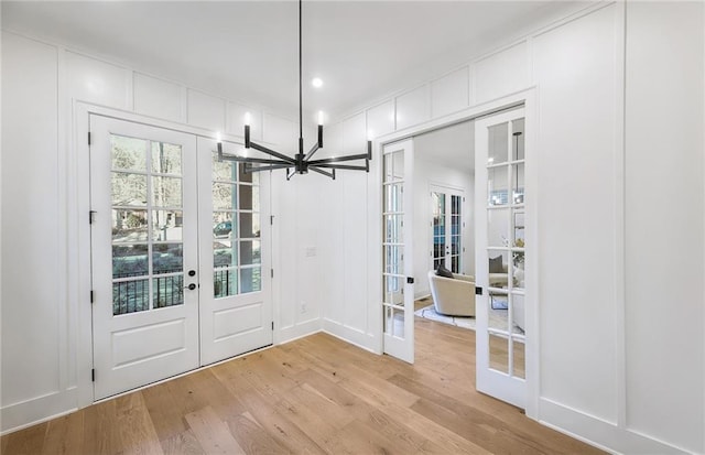 doorway to outside featuring french doors, a chandelier, and light wood-type flooring