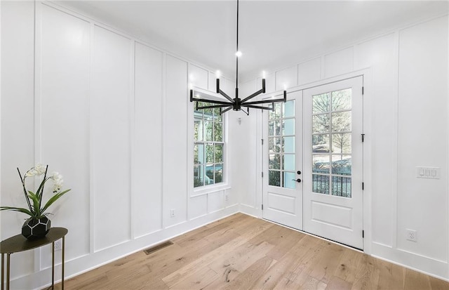 doorway with light wood-type flooring, french doors, a notable chandelier, and a wealth of natural light