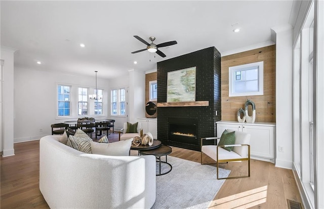 living room featuring ceiling fan with notable chandelier, a fireplace, and light hardwood / wood-style floors