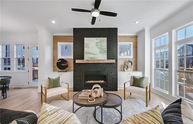 living room featuring a brick fireplace, light wood-type flooring, ceiling fan, and crown molding