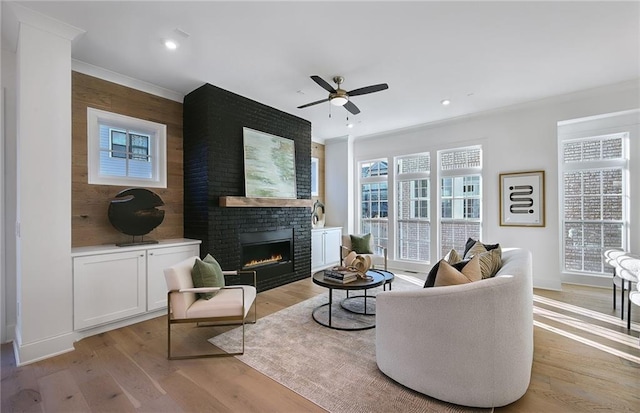 living room with ceiling fan, a brick fireplace, ornamental molding, and light hardwood / wood-style floors