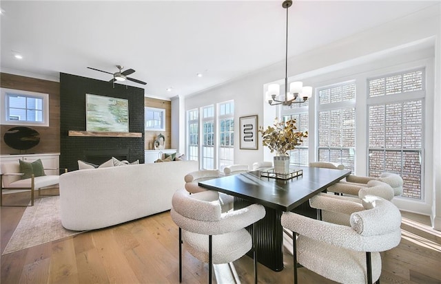 dining space with ceiling fan with notable chandelier, a brick fireplace, and light hardwood / wood-style floors