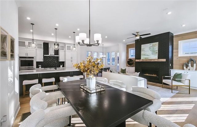 dining area featuring ceiling fan with notable chandelier, sink, a fireplace, and light wood-type flooring