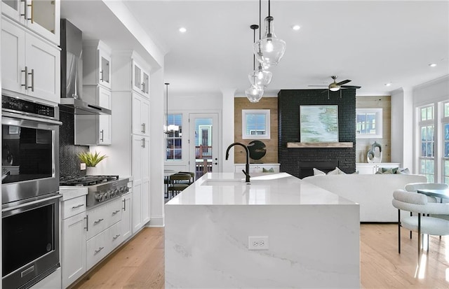 kitchen with white cabinets, decorative light fixtures, a kitchen island with sink, and appliances with stainless steel finishes