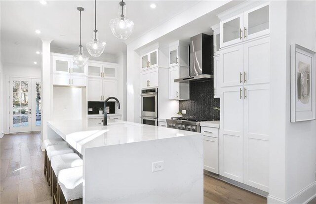 kitchen with white cabinetry, a kitchen island with sink, and wall chimney exhaust hood