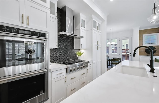 kitchen featuring decorative light fixtures, stainless steel appliances, wall chimney exhaust hood, and white cabinets