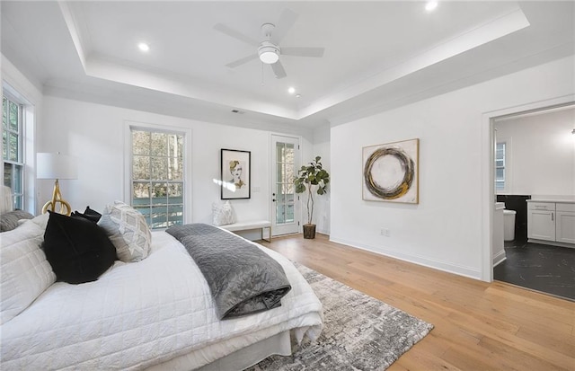 bedroom with ceiling fan, light wood-type flooring, ensuite bath, and a tray ceiling